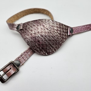 May include: A purple leather eye patch with a textured surface and a brown leather strap with a buckle.