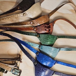 May include: A set of nine leather eye patches in various colors and patterns, including brown, beige, tan, orange, green, blue, and navy. Each patch has a strap for wearing.
