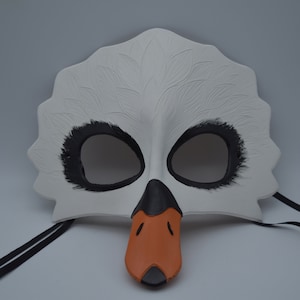 Op de afbeelding: Witte zwanenmasker met zwarte ooggaten en een oranje snavel. Het masker heeft zwarte veren rond de ogen en is bevestigd aan zwarte lintjes.