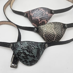 May include: Three leather eye patches with different snake skin patterns. The eye patches are attached to black leather straps.