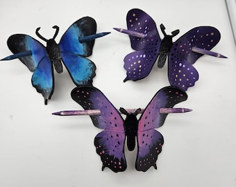 May include: Three decorative butterfly hair pins. One butterfly is blue, the second is purple with yellow dots, and the third is purple with black spots. Each butterfly has a wooden pin through its body.