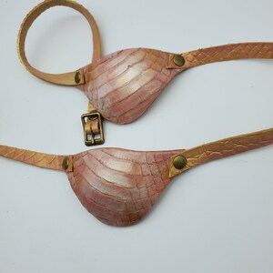 May include: A pair of pink leather eye patches with gold accents and a buckle fastening. The eye patches are attached to a brown leather strap.