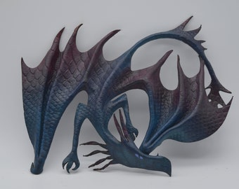 Puede incluir: Escultura de dragón artesanal con alas extendidas. El dragón presenta un cuerpo texturizado y escamado en tonos azules y morados. Una pieza única de arte fantástico.