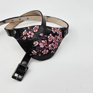 May include: Black leather eye patch with a painted design of pink cherry blossoms.