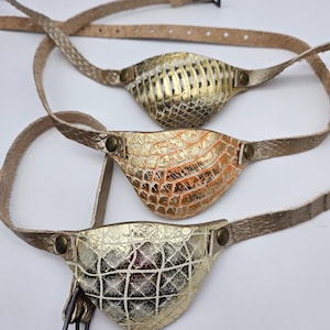 May include: Three leather eye patches with gold and orange accents. The eye patches are made of textured leather and have a strap for attaching to the head.