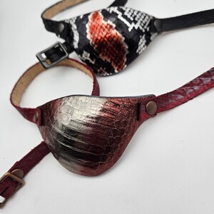 May include: Two leather eye patches. One is black with a red and white snake skin pattern. The other is burgundy with a silver metallic finish.