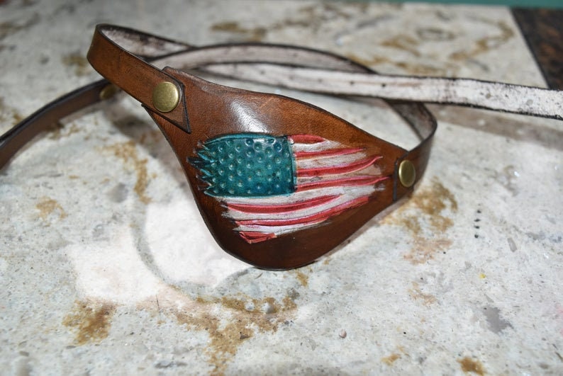 Op de afbeelding: Een bruin leren ooglapje met een rood, wit en blauw Amerikaans vlagontwerp.
