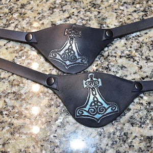 May include: Two black leather eye patches with a silver Mjolnir hammer design. The hammer is surrounded by a Celtic knot design.