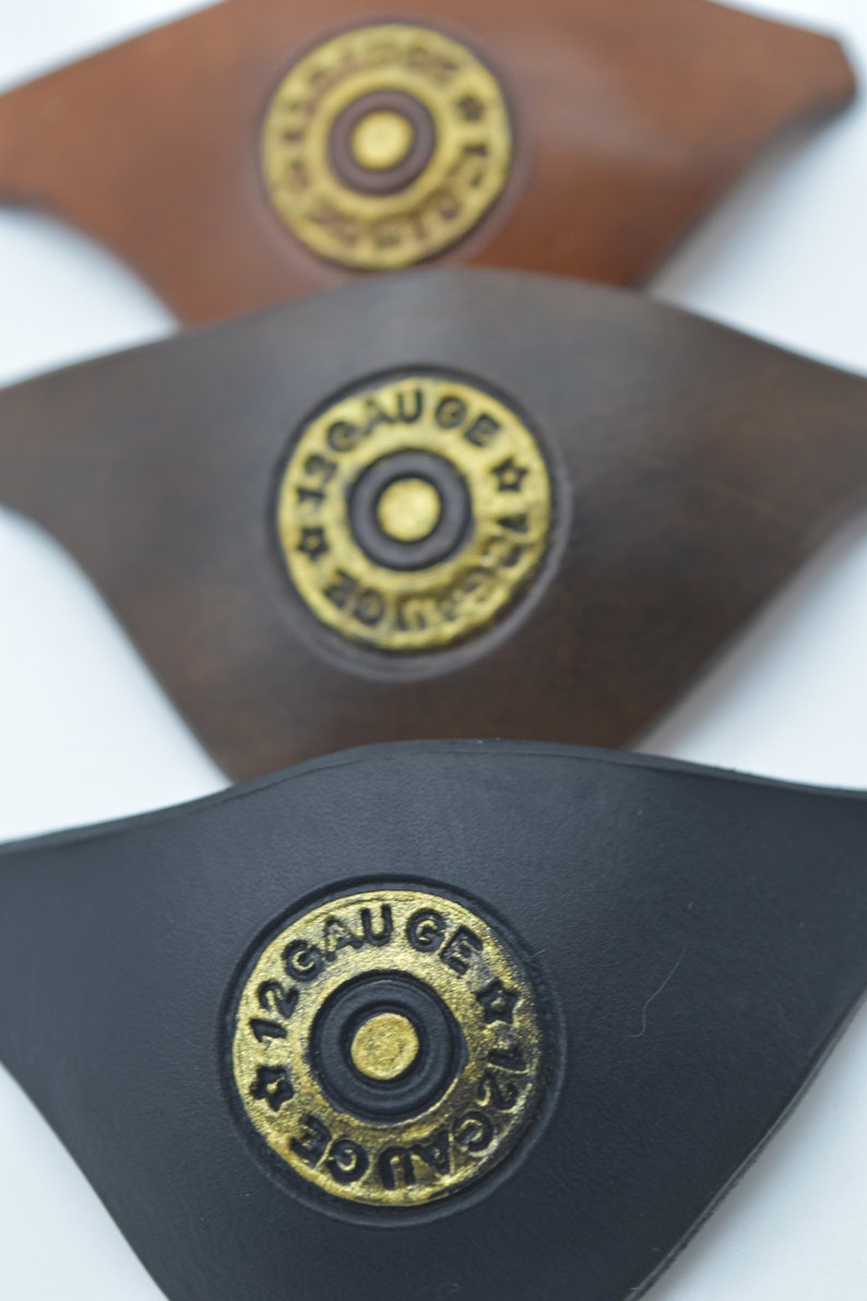 K&ouml;nnte beinhalten: Drei Leder-Patches mit einem 12 Gauge-Schrotflintenpatronen-Design. Die Patches sind braun, dunkelbraun und schwarz.