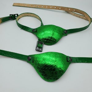 May include: Two green eye patches with a textured, crocodile-like pattern. Each patch has a strap and a buckle for adjustment. The eye patches are made of a shiny, metallic green material.