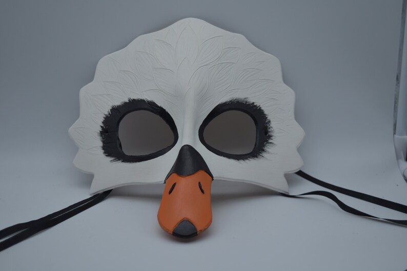 Op de afbeelding: Witte zwanenmasker met zwarte ooggaten en een oranje snavel. Het masker heeft zwarte banden.