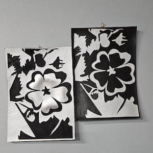 May include: Two rectangular wall art pieces featuring high-contrast black and white floral patterns. Each piece displays a large central flower with stylized petals and surrounding foliage, rendered in a bold, graphic, two-tone color scheme.