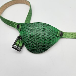 May include: A green leather eye patch with a honeycomb pattern. The patch is attached to a green leather strap with a black buckle.