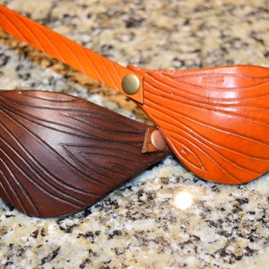May include: Two leather eye patches with a wood grain pattern. The eye patch on the left is brown and the eye patch on the right is orange.