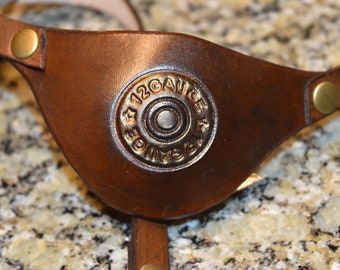 May include: A brown leather eye patch with a gold-colored 12 gauge shotgun shell casing embossed on the front.