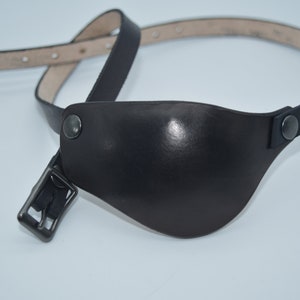 May include: A black leather eye patch with a strap and buckle. The eye patch is made of soft, supple leather and has a smooth, polished finish.
