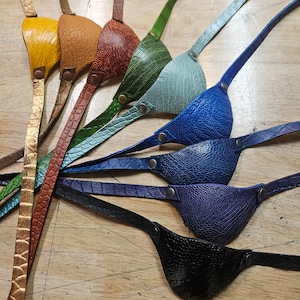 May include: Seven leather eye patches in various colours, including yellow, orange, brown, green, blue, and black. Each patch has a strap for wearing.