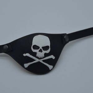 May include: A black leather pirate eye patch with a white skull and crossbones design.