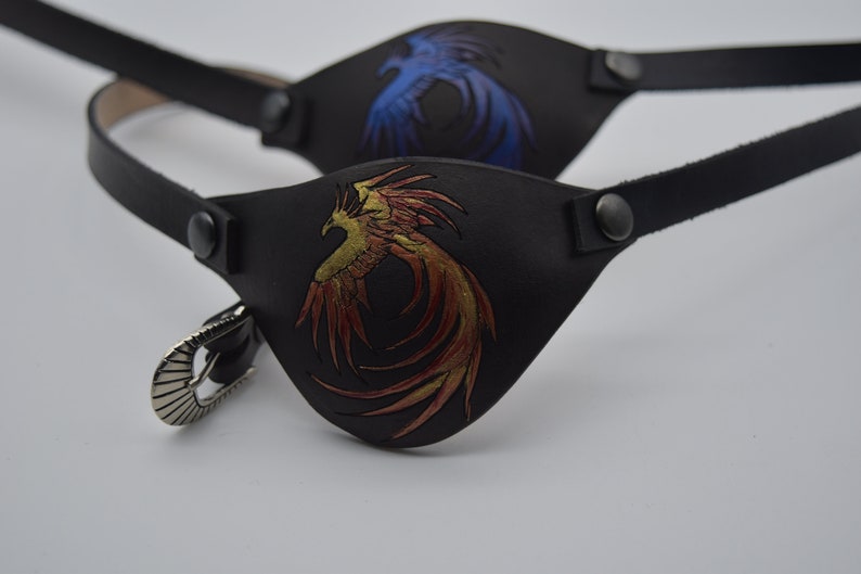 Puede incluir: Dos parches para ojos de cuero negro con correas ajustables. Un parche presenta un dise&ntilde;o de f&eacute;nix dorado y rojo, mientras que el otro presenta un dise&ntilde;o de f&eacute;nix azul.