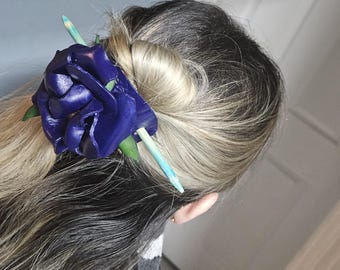 May include: A dark blue leather rose hair clip with a wooden stick. The clip is in a woman's hair.
