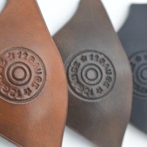 K&ouml;nnte beinhalten: Drei Leder-Patches in Braun, Dunkelbraun und Schwarz mit dem Text "#12 GAUGE" in einem Kreis gepr&auml;gt.