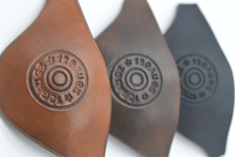 K&ouml;nnte beinhalten: Drei Leder-Patches in Braun, Dunkelbraun und Schwarz mit dem Text "#12 GAUGE" in einem Kreis gepr&auml;gt.
