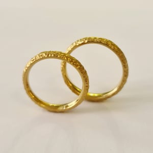 Könnte beinhalten: Zwei goldene Eheringe mit einer strukturierten Oberfläche. Die Ringe sind ineinander verschlungen.