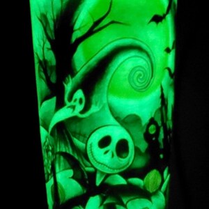 K&ouml;nnte beinhalten: Ein gr&uuml;ner, im Dunkeln leuchtender Becher mit einer Schwarzwei&szlig;illustration von Jack Skellington aus Nightmare Before Christmas. Die Illustration zeigt einen gruseligen Baum, einen Halbmond und ein wirbelndes Muster.
