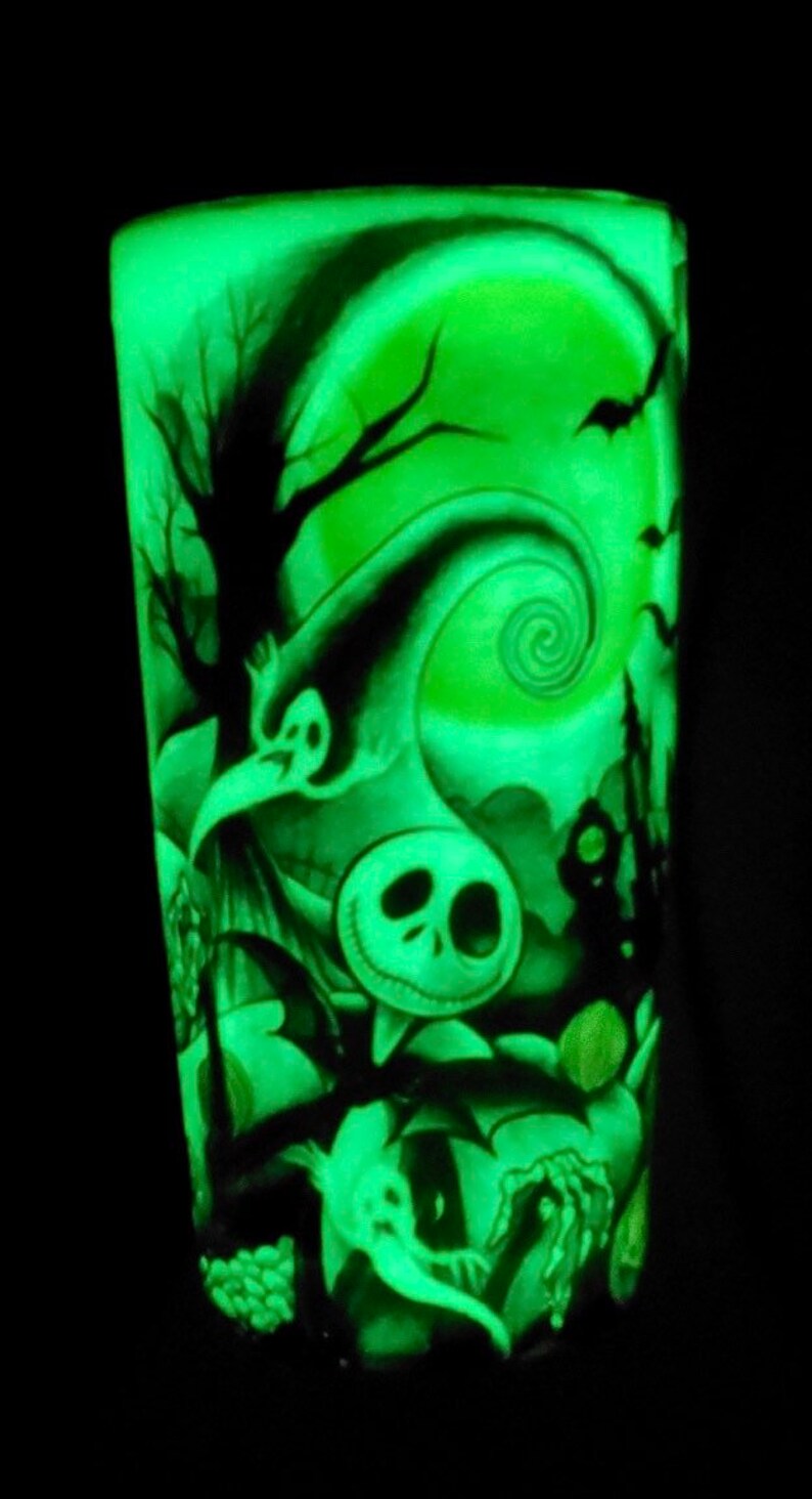 K&ouml;nnte beinhalten: Ein gr&uuml;ner, im Dunkeln leuchtender Becher mit einer Schwarzwei&szlig;illustration von Jack Skellington aus Nightmare Before Christmas. Die Illustration zeigt einen gruseligen Baum, einen Halbmond und ein wirbelndes Muster.