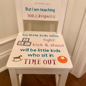 May include: White wooden child's chair with text that reads "Kids will be Kids" and "TIME OUT". The seat features a rocking horse and ABC blocks graphic. The chair is designed for children's use.
