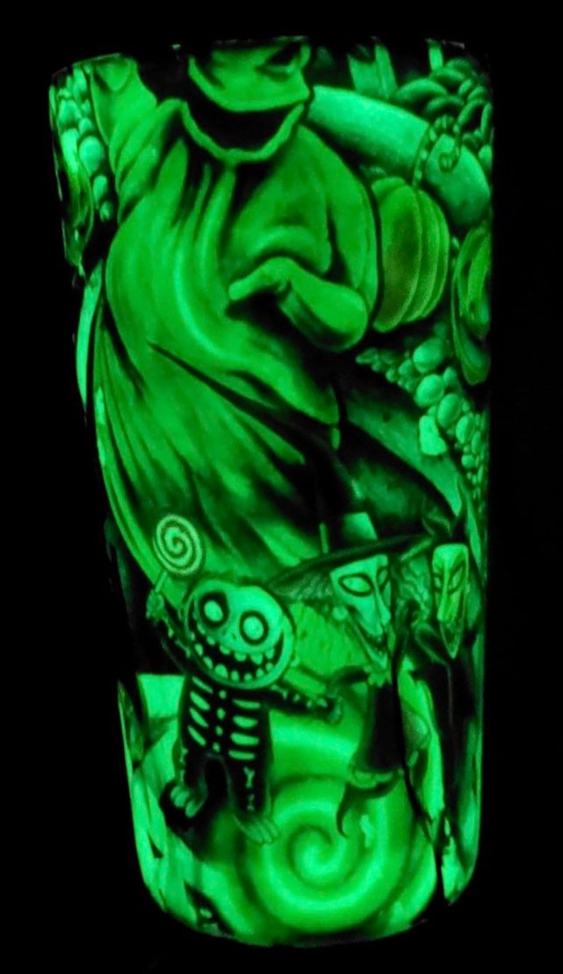 K&ouml;nnte beinhalten: Ein gr&uuml;ner, im Dunkeln leuchtender Becher mit einem Motiv von Figuren aus Nightmare Before Christmas. Die Figuren sind Jack Skellington, Sally und Oogie Boogie.
