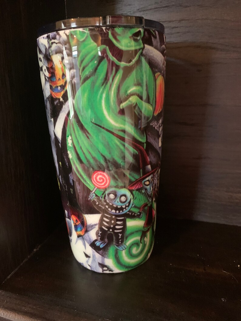 K&ouml;nnte beinhalten: Ein gr&uuml;ner und schwarzer Edelstahlbecher mit einem grafischen Aufdruck von Figuren aus Nightmare Before Christmas. Die Figuren sind Jack Skellington, Sally und Oogie Boogie.