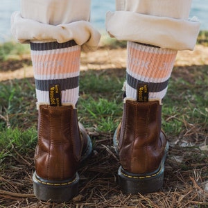 May include: Brown leather Chelsea boots with black soles and white fuzzy lining. The boots are worn with striped socks that say "With Soles Bouncing" in yellow text.