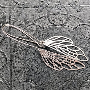 May include: A pair of silver earrings with a delicate dragonfly design. The earrings are made of metal and have a simple, elegant style.