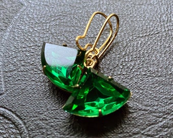 May include: A pair of gold earrings with large, faceted, emerald green stones. The stones are shaped like a fan.
