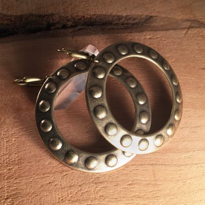 May include: A pair of gold-toned hoop earrings with a textured, circular design. The earrings have a hammered finish and are accented with small, raised dots.