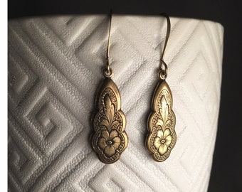 May include: A pair of gold-tone dangle earrings with a floral design. The earrings are made of metal and have a teardrop shape.
