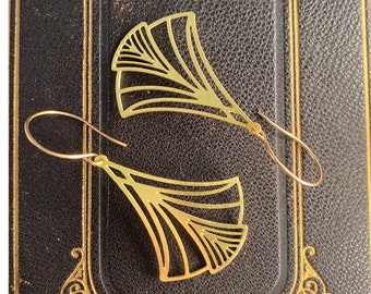 May include: A pair of gold-tone earrings with a geometric fan-shaped design. The earrings are made of metal and have a delicate, intricate design.