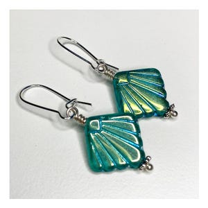 May include: A pair of silver earrings with iridescent teal blue and green glass teardrop-shaped pendants. The pendants have a fan-like design.
