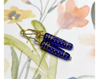 May include: A pair of blue glass earrings with gold accents and a dotted pattern. The earrings are dangle style with a gold hook.