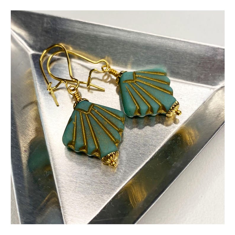 May include: A pair of gold earrings with teal blue fan-shaped glass beads. The beads have a gold-toned pattern.