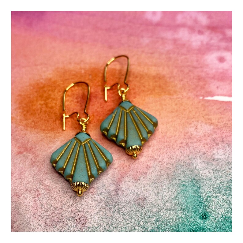May include: A pair of gold earrings with a teal blue and gold geometric design. The earrings are shaped like a fan or a shell.