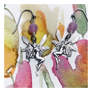 May include: A pair of silver fairy earrings with lavender glass beads. The fairies are depicted with wings and flowing hair.