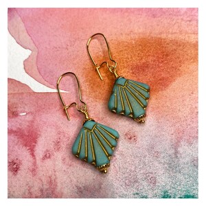 May include: A pair of gold earrings with a teal blue geometric design. The earrings have a fan-shaped design with gold accents.