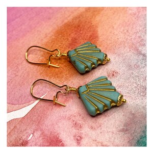 May include: A pair of gold earrings with a teal blue geometric design. The earrings have a fan-shaped design with gold accents.