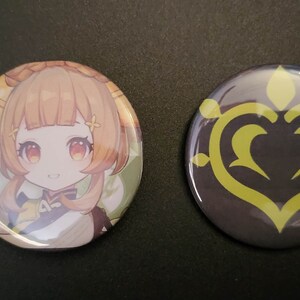 May include: Two round pinback buttons. One button features a cartoon illustration of a young girl with long orange hair wearing a white and yellow outfit. The other button features a yellow stylized heart design on a dark gray background.