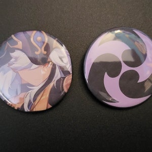May include: Two round button pins. One features a character with white hair and a purple and gold hat. The other pin has a purple and black swirl design.