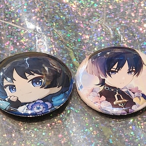 May include: Two round, glossy buttons featuring anime-style character illustrations. One button depicts a character with dark hair and blue eyes, while the other shows a character with a similar style and color palette. The buttons are set against a sparkly background.