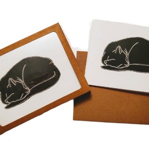 May include: Two greeting cards with brown envelopes. Each card features a black silhouette of a cat sleeping on a white background.