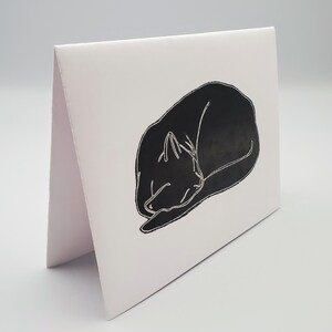 May include: A black and white illustration of a cat curled up asleep on a white card.